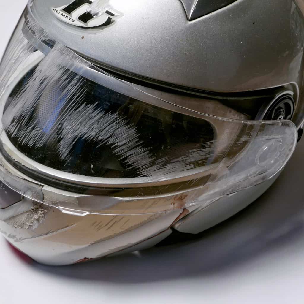 A silver motorcycle helmet with scratches from an accident on a clear visor.